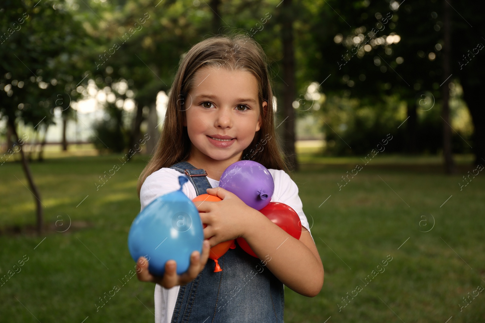 Photo of Cute little girl holding water bombs in park
