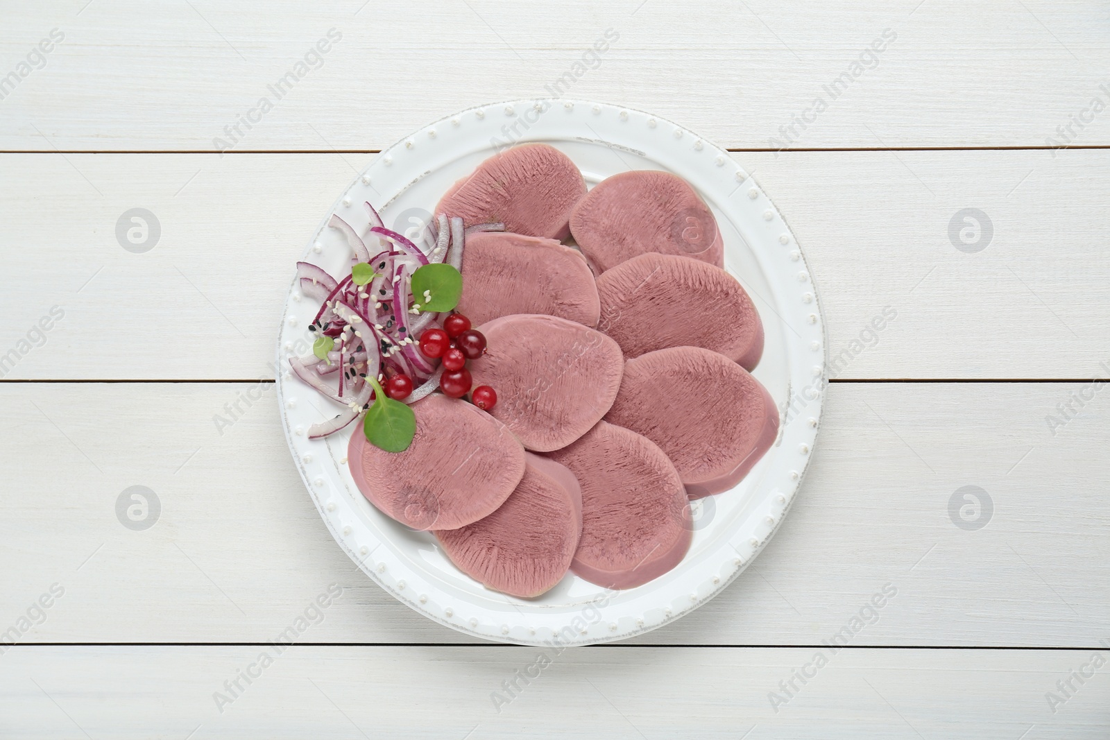 Photo of Tasty beef tongue pieces, berries and red onion on white wooden table, top view