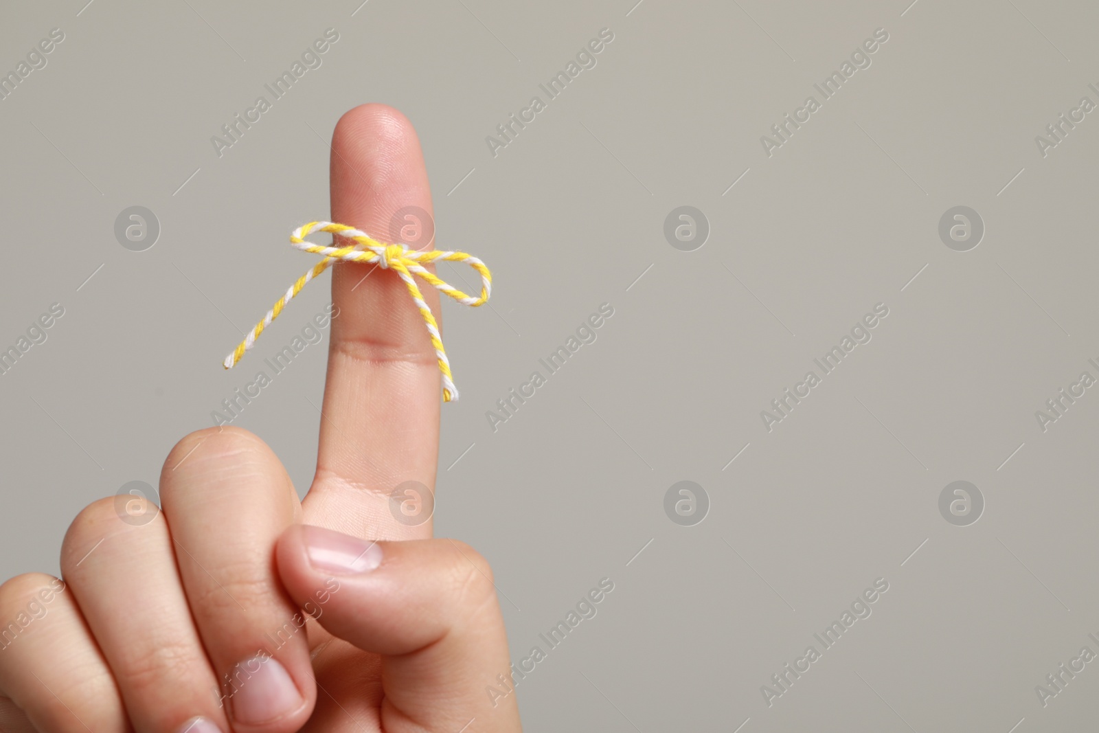 Photo of Man showing index finger with tied bow as reminder on light grey background, closeup. Space for text