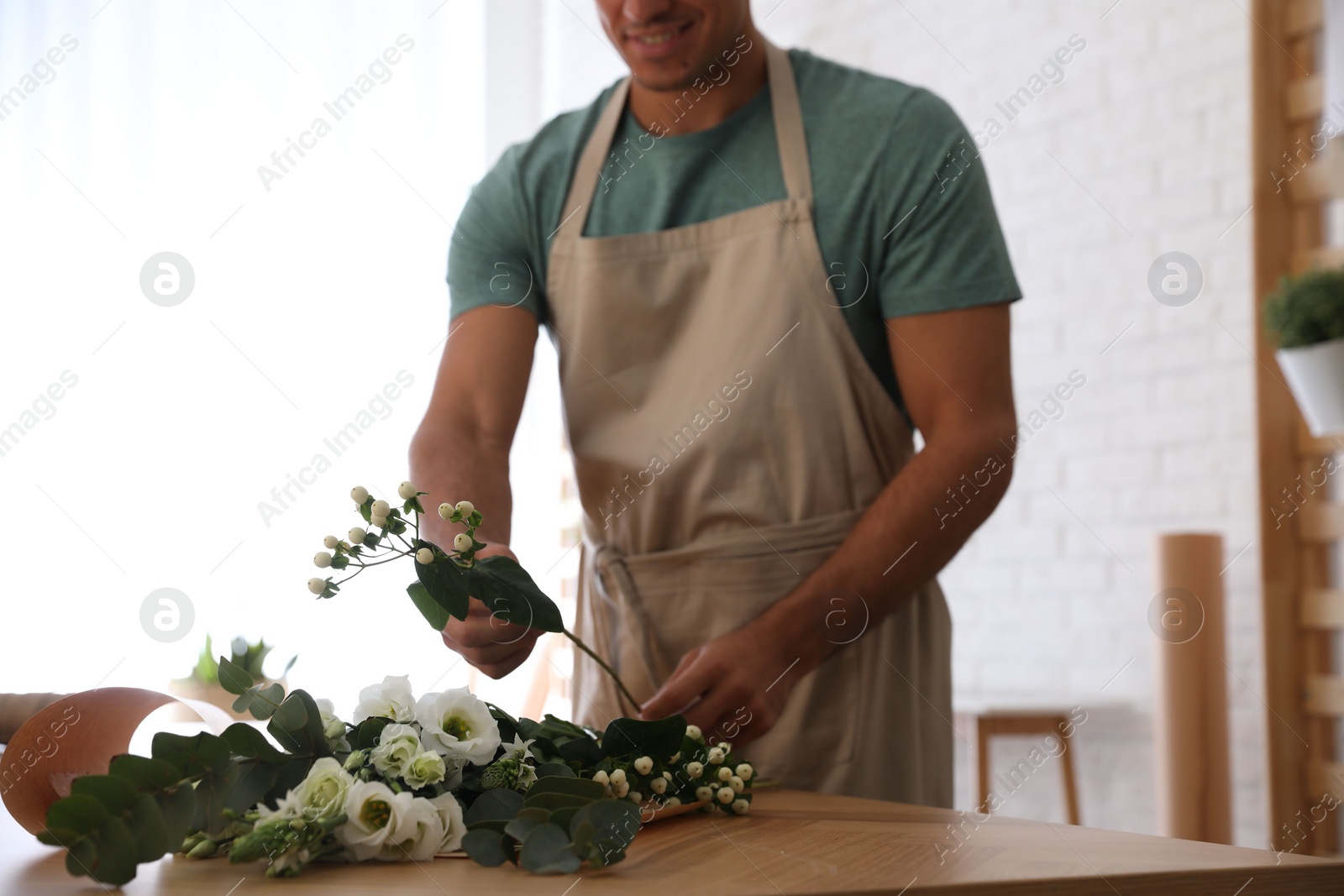 Photo of Florist making beautiful bouquet at table in workshop, closeup