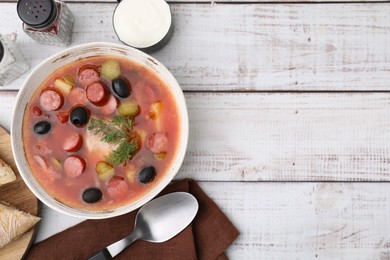 Photo of Meat solyanka soup with thin dry smoked sausages served on white wooden table, flat lay. Space for text