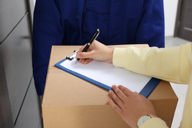 Photo of Woman signing for delivered parcel from courier indoors, closeup