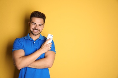 Photo of Happy young man with air conditioner remote control on yellow background. Space for text