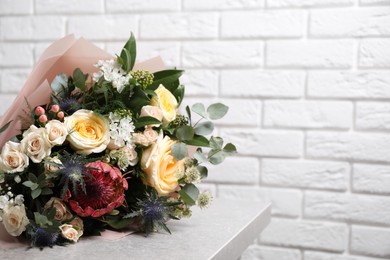 Beautiful bouquet with roses on light table near white brick wall. Space for text