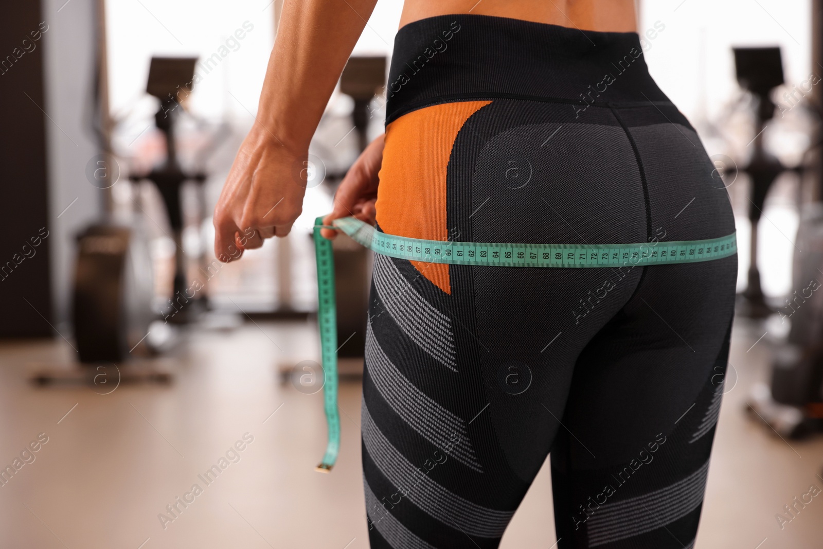 Photo of Woman measuring hips with tape in gym, closeup