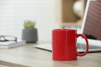 Photo of Red ceramic mug and laptop on wooden table indoors. Space for text