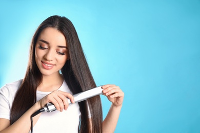 Happy woman using hair iron on color background. Space for text