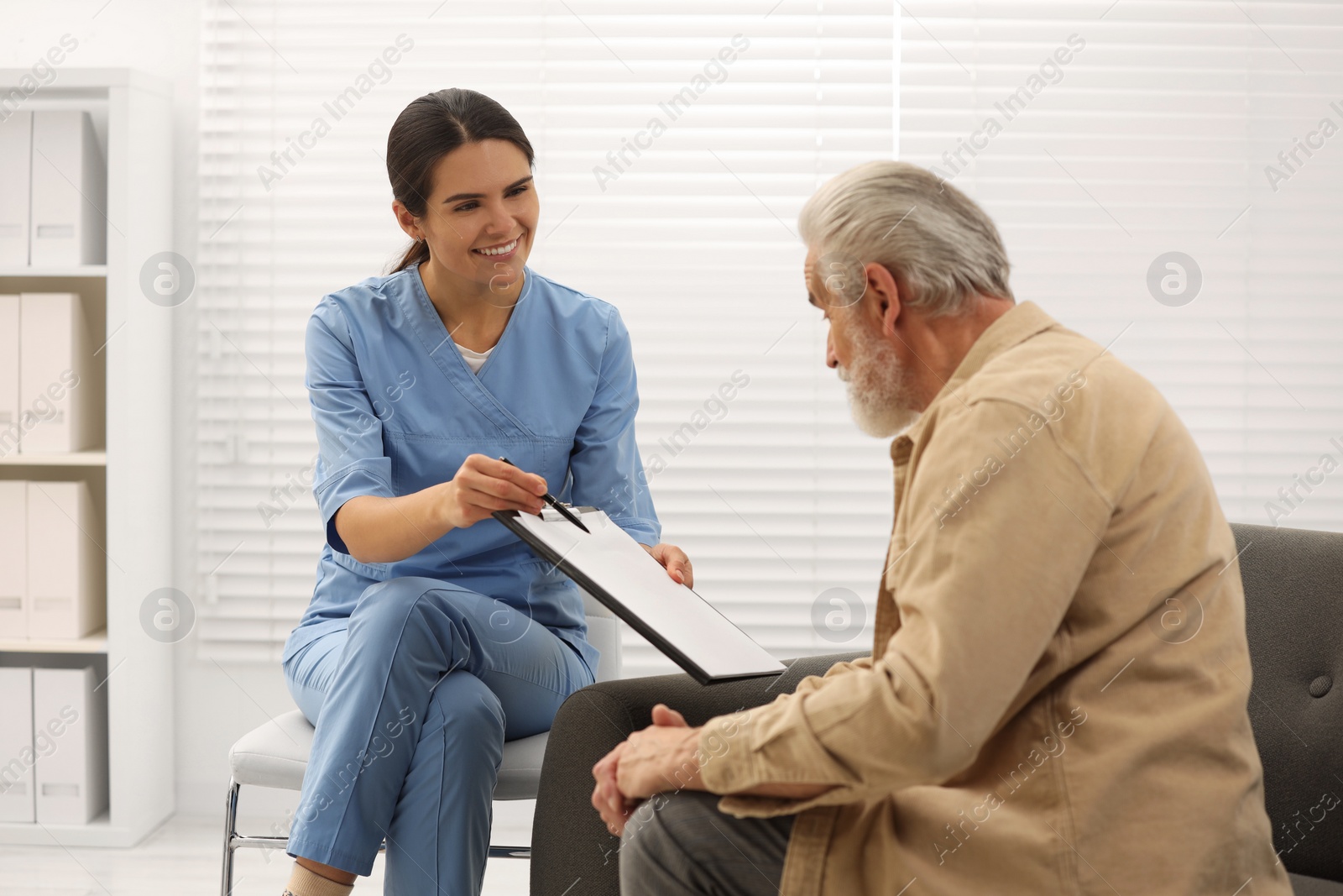 Photo of Smiling nurse with clipboard and elderly patient in hospital