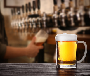 Image of Fresh cold beer on wooden table and bartender in pub, space for text 