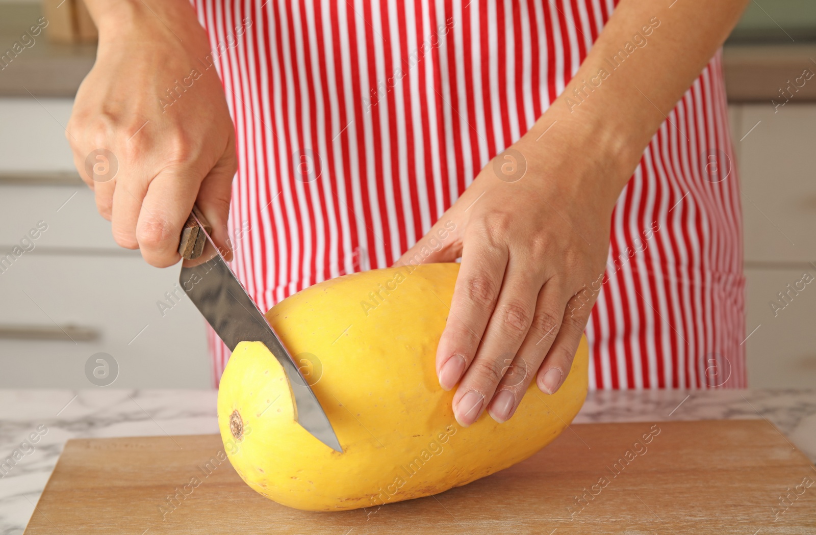 Photo of Woman cutting ripe spaghetti squash on table in kitchen, closeup