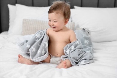 Happy baby boy with blanket sitting on bed at home