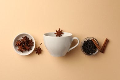 Cup with anise stars, dry tea and cinnamon sticks on beige background, flat lay