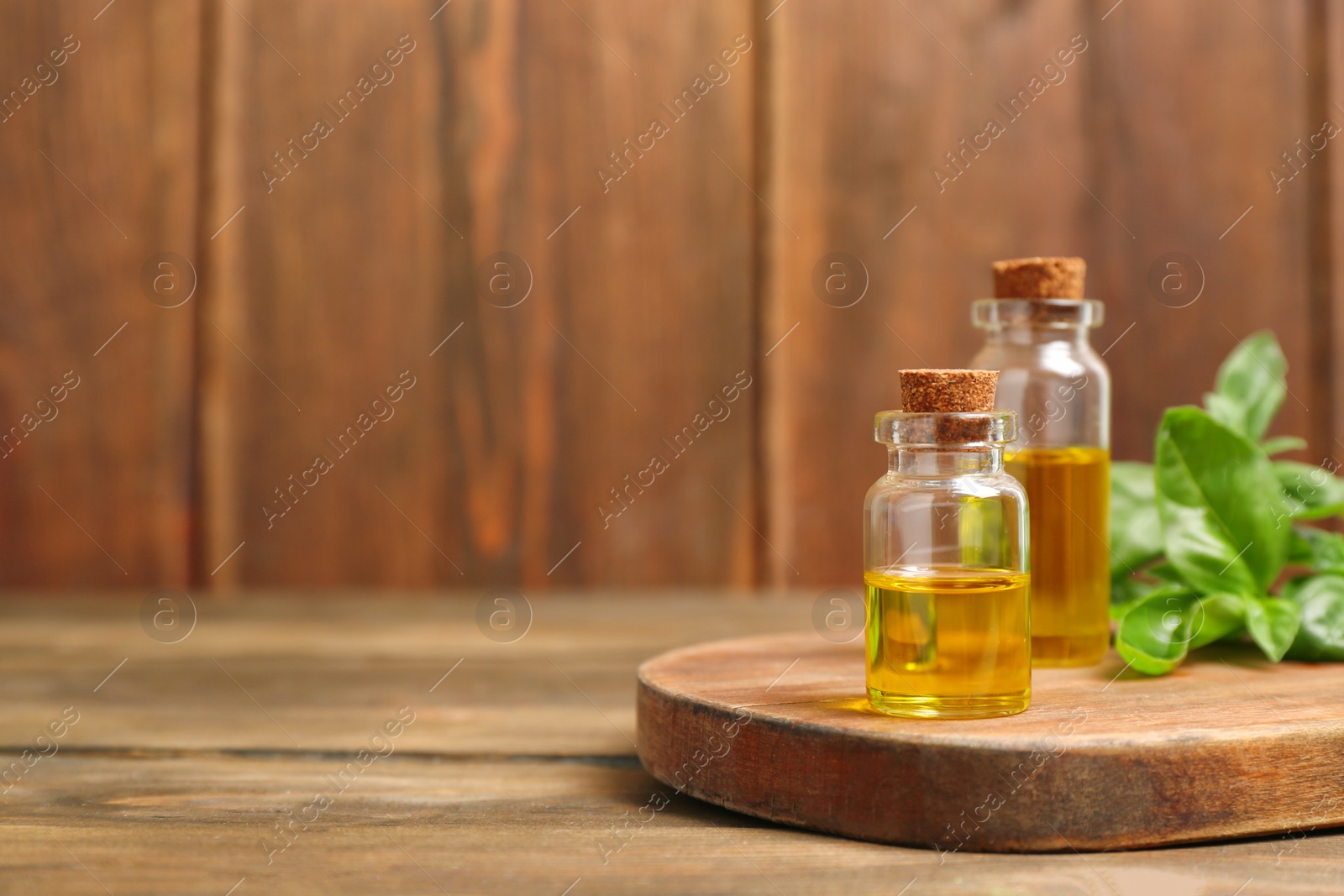 Photo of Wooden board with basil oil in glass bottles. Space for text