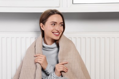 Photo of Woman with blanket sitting near heating radiator indoors