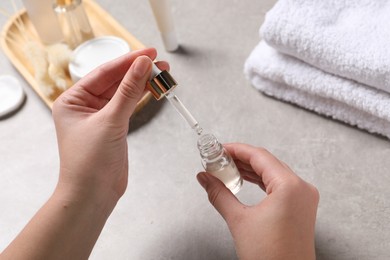 Photo of Woman with bottle of cosmetic serum and pipette at light table, closeup