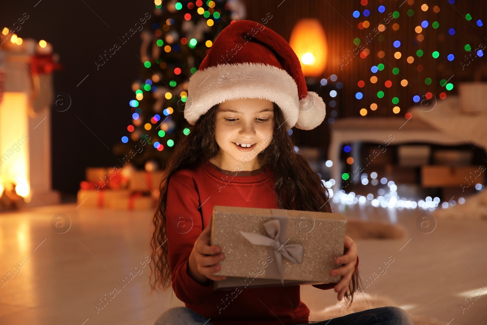 Photo of Cute little child in Santa hat with Christmas gift box at home