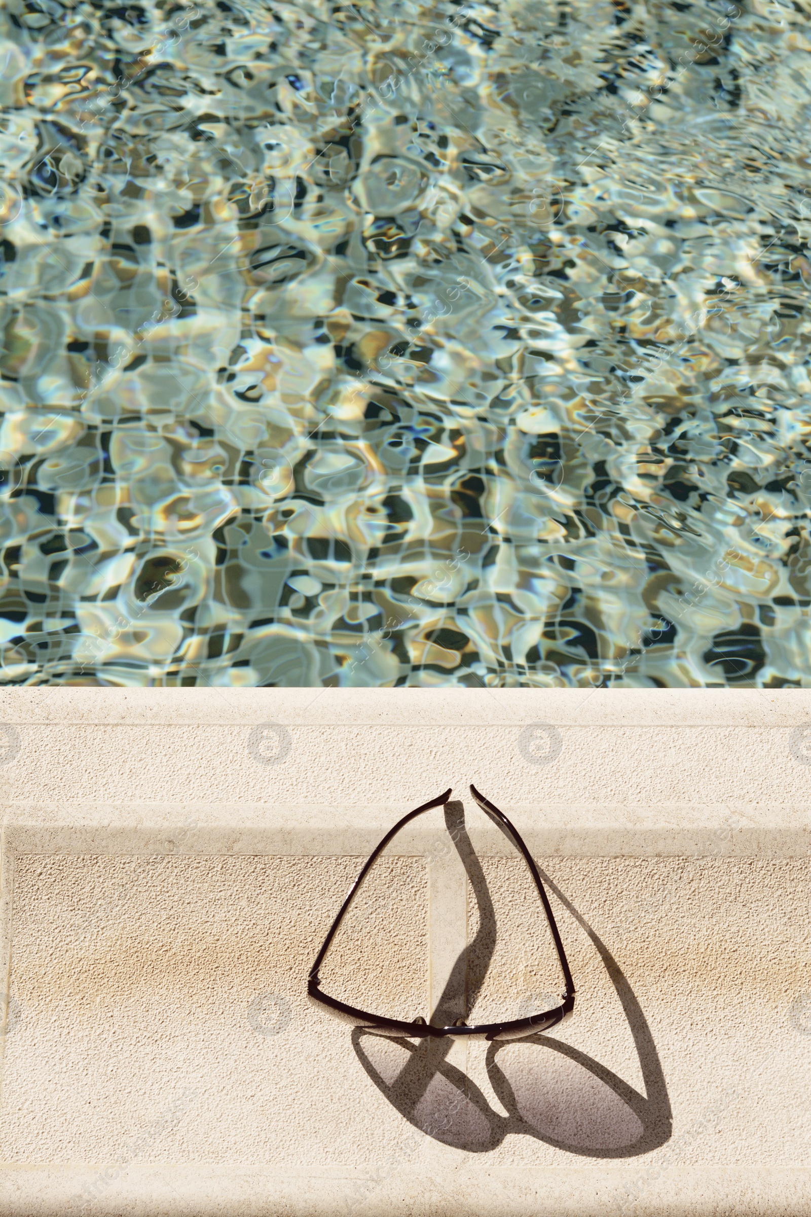 Photo of Stylish sunglasses near outdoor swimming pool on sunny day, top view. Space for text