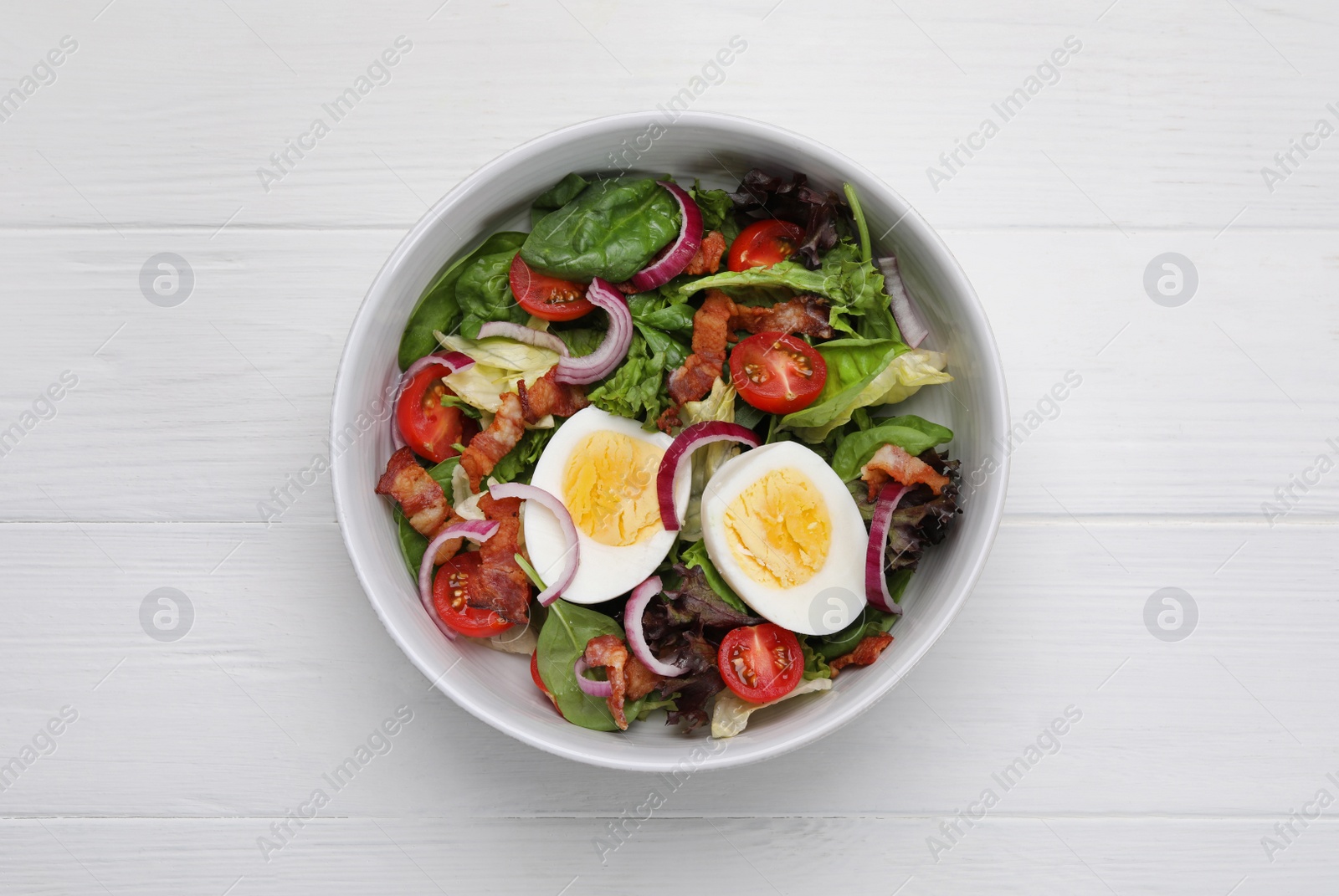 Photo of Delicious salad with boiled egg, bacon and vegetables on white wooden table, top view
