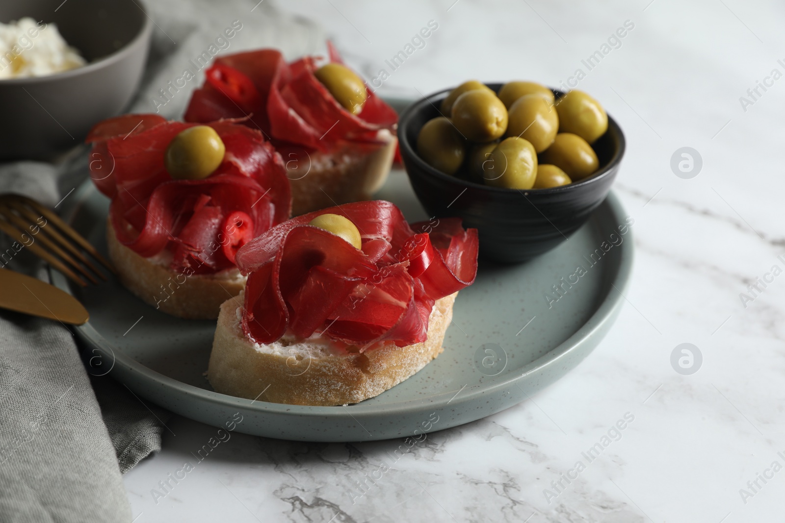 Photo of Delicious sandwiches with bresaola, cream cheese and olives served on white marble table, closeup