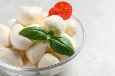 Photo of Delicious mozzarella balls and basil leaves in glass bowl on light gray table, closeup