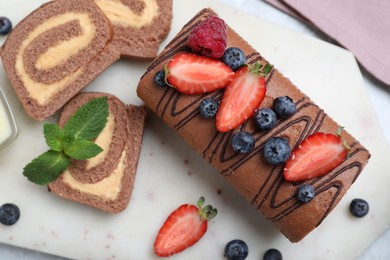 Tasty chocolate cake roll with cream and berries on light grey marble table, flat lay