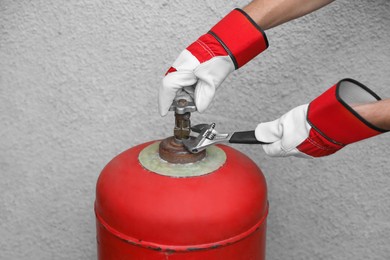 Photo of Worker with adjustable wrench opening red gas cylinder near wall, closeup