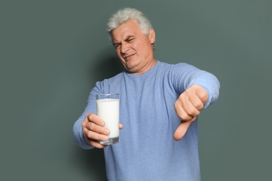 Mature man with dairy allergy holding glass of milk on color background