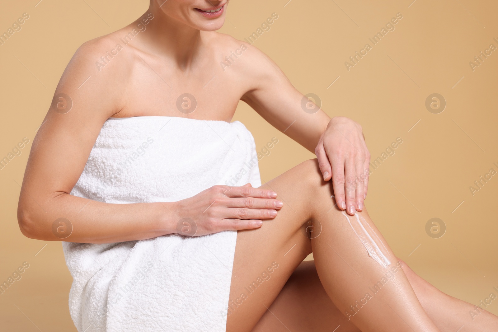 Photo of Woman applying body cream onto her leg against beige background, closeup