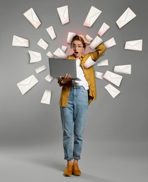 Image of Email spam. Emotional young woman with laptop and many letters on grey background
