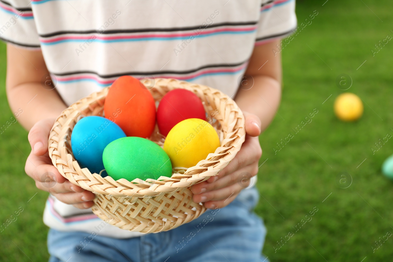 Photo of Cute little boy with basket full of Easter eggs outdoors, closeup