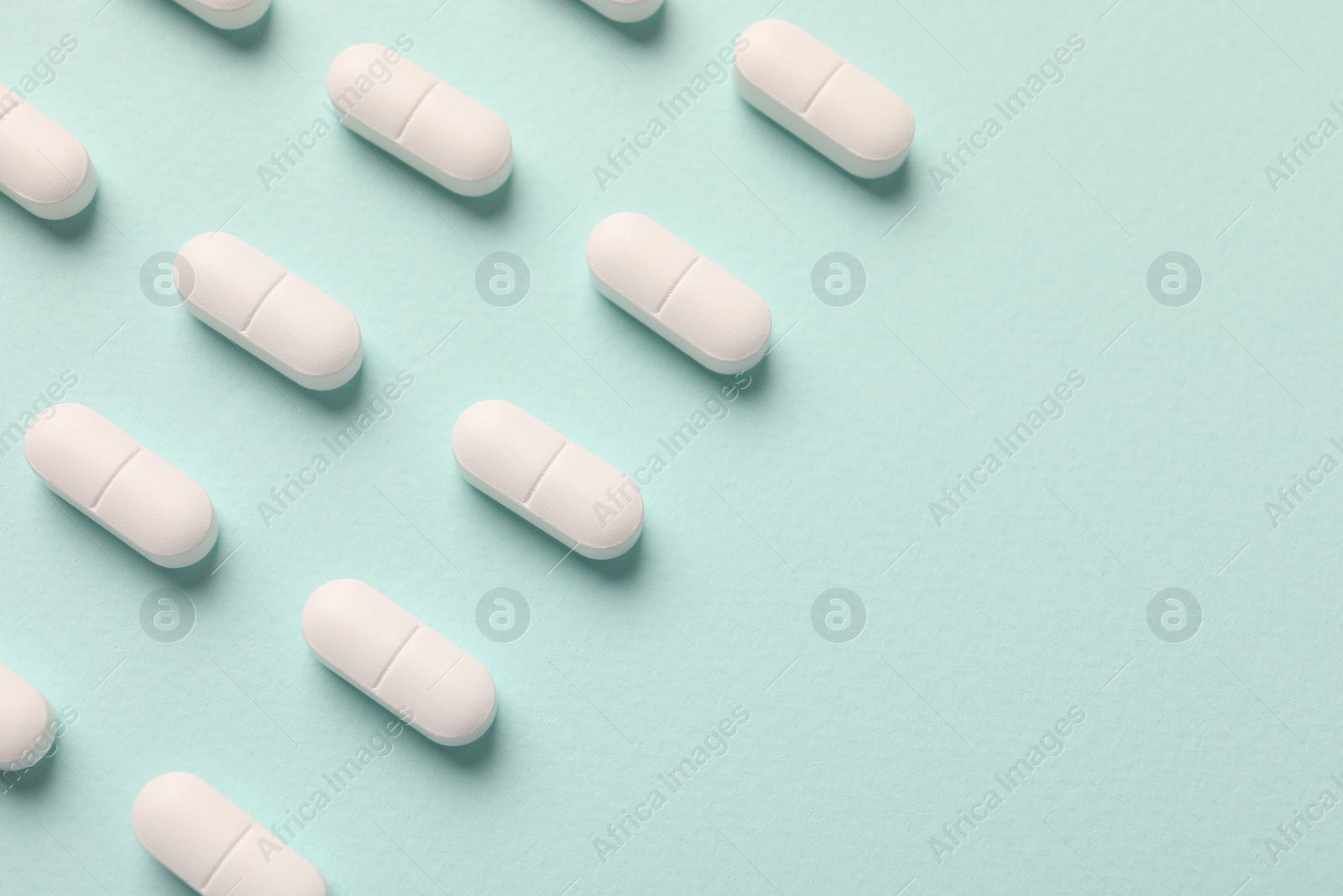 Photo of White pills on mint background, flat lay. Space for text