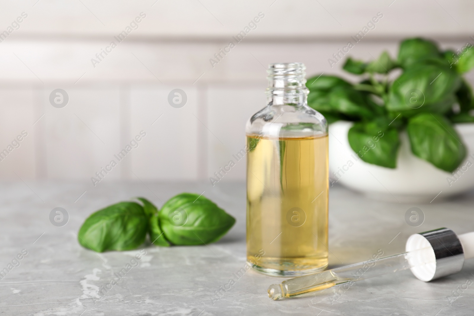 Photo of Glass bottle of essential oil, dropper and basil on table