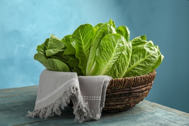 Photo of Wicker basket with fresh ripe cos lettuce on wooden table