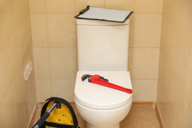 Photo of Pipe wrench and clipboard on toilet indoors