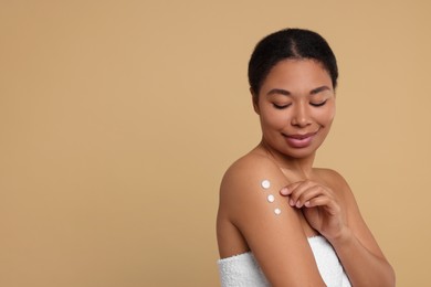 Photo of Young woman applying body cream onto shoulder on beige background. Space for text