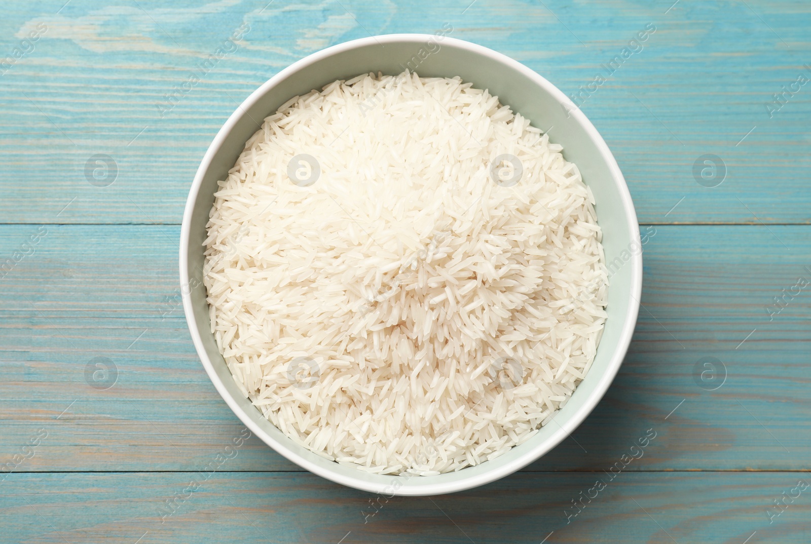 Photo of Raw basmati rice in bowl on light blue wooden table, top view