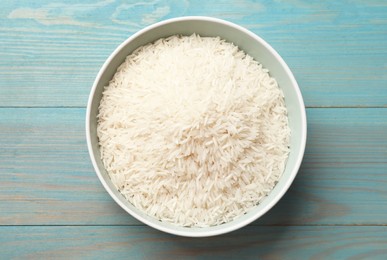 Photo of Raw basmati rice in bowl on light blue wooden table, top view