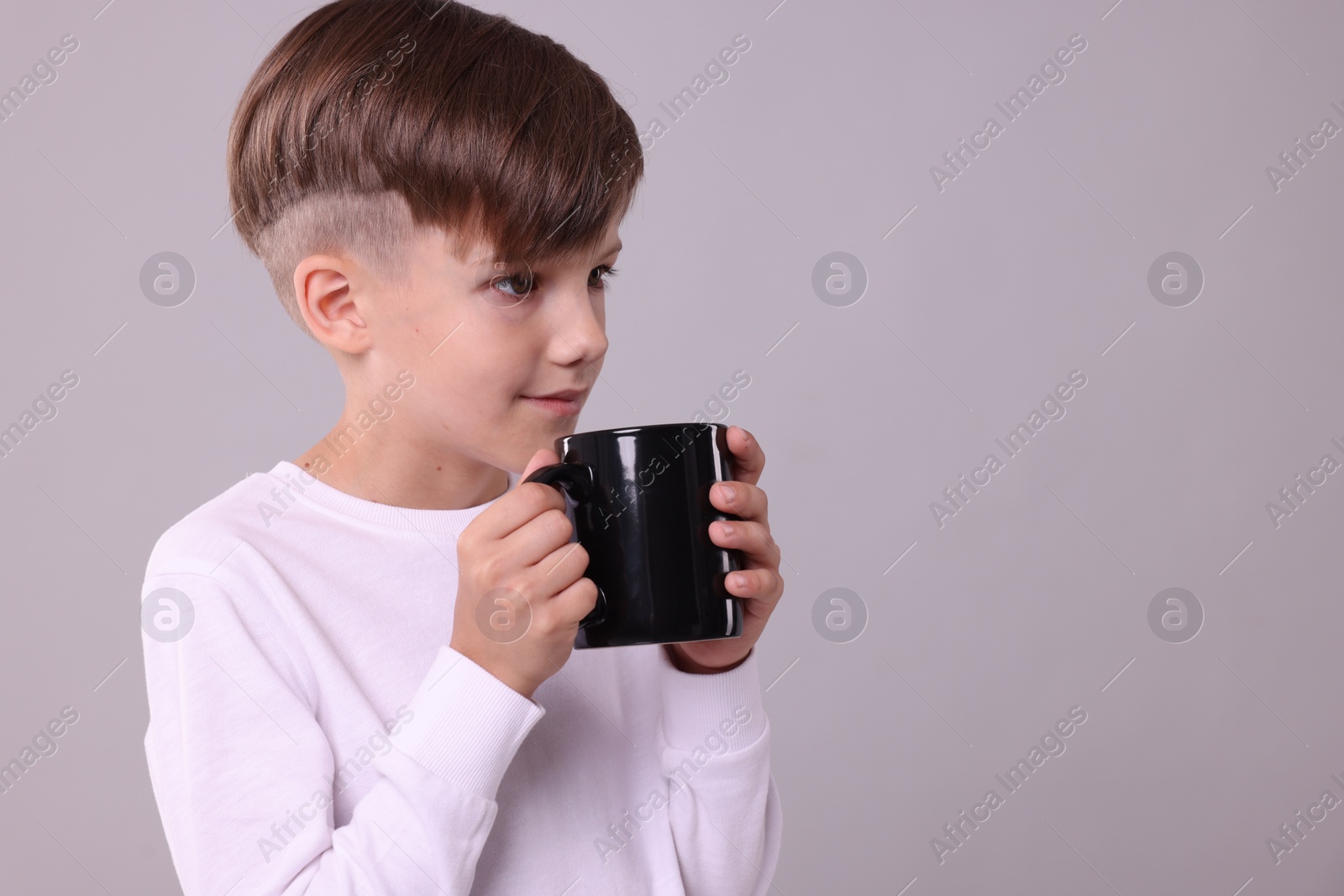 Photo of Cute boy with black ceramic mug on light grey background, space for text