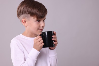 Cute boy with black ceramic mug on light grey background, space for text