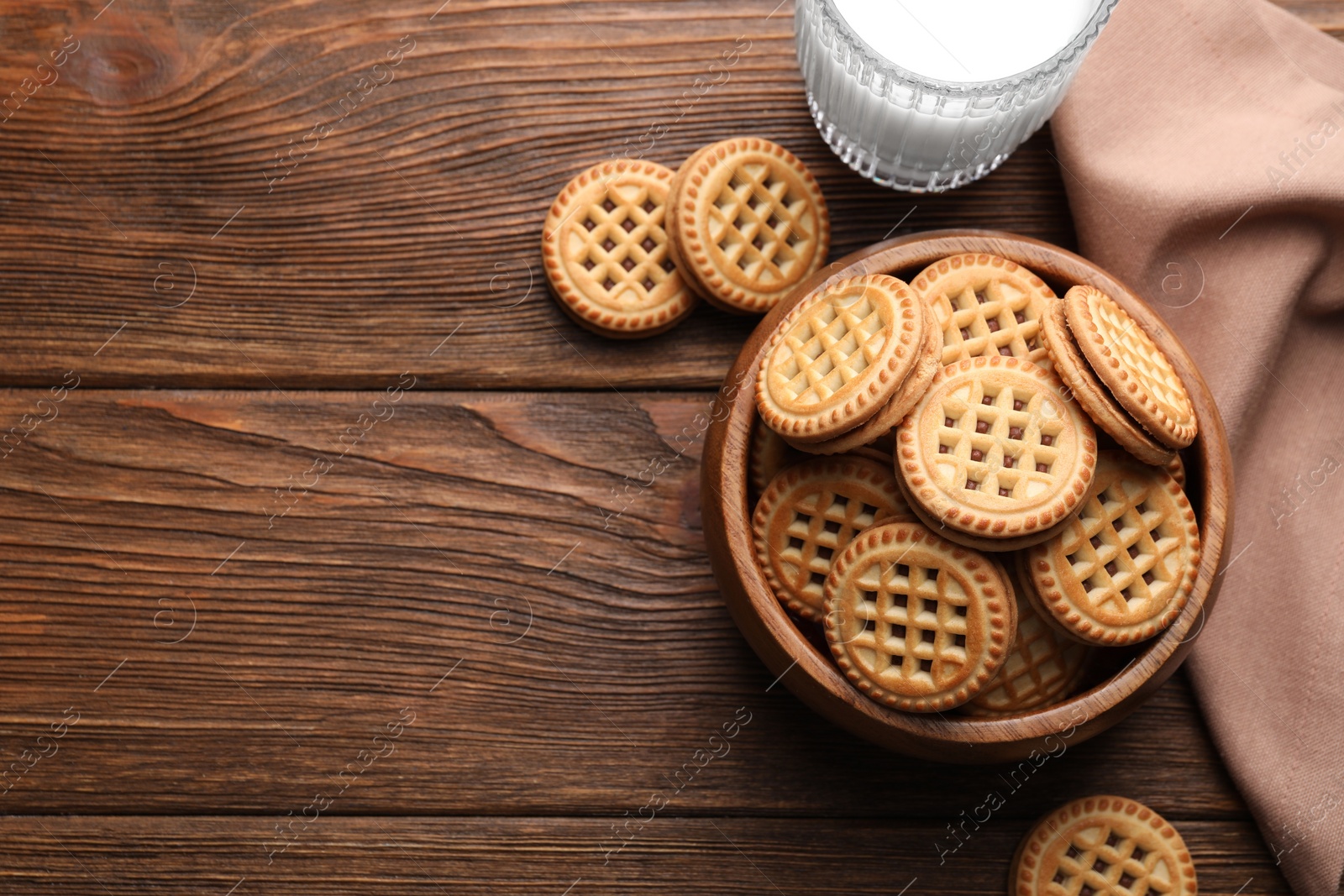 Photo of Tasty sandwich cookies with cream and glass of milk on wooden table, flat lay. Space for text