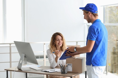 Young woman signing for delivered parcel in office. Courier service