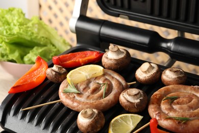 Photo of Electric grill with homemade sausages, bell pepper and mushrooms on table, closeup