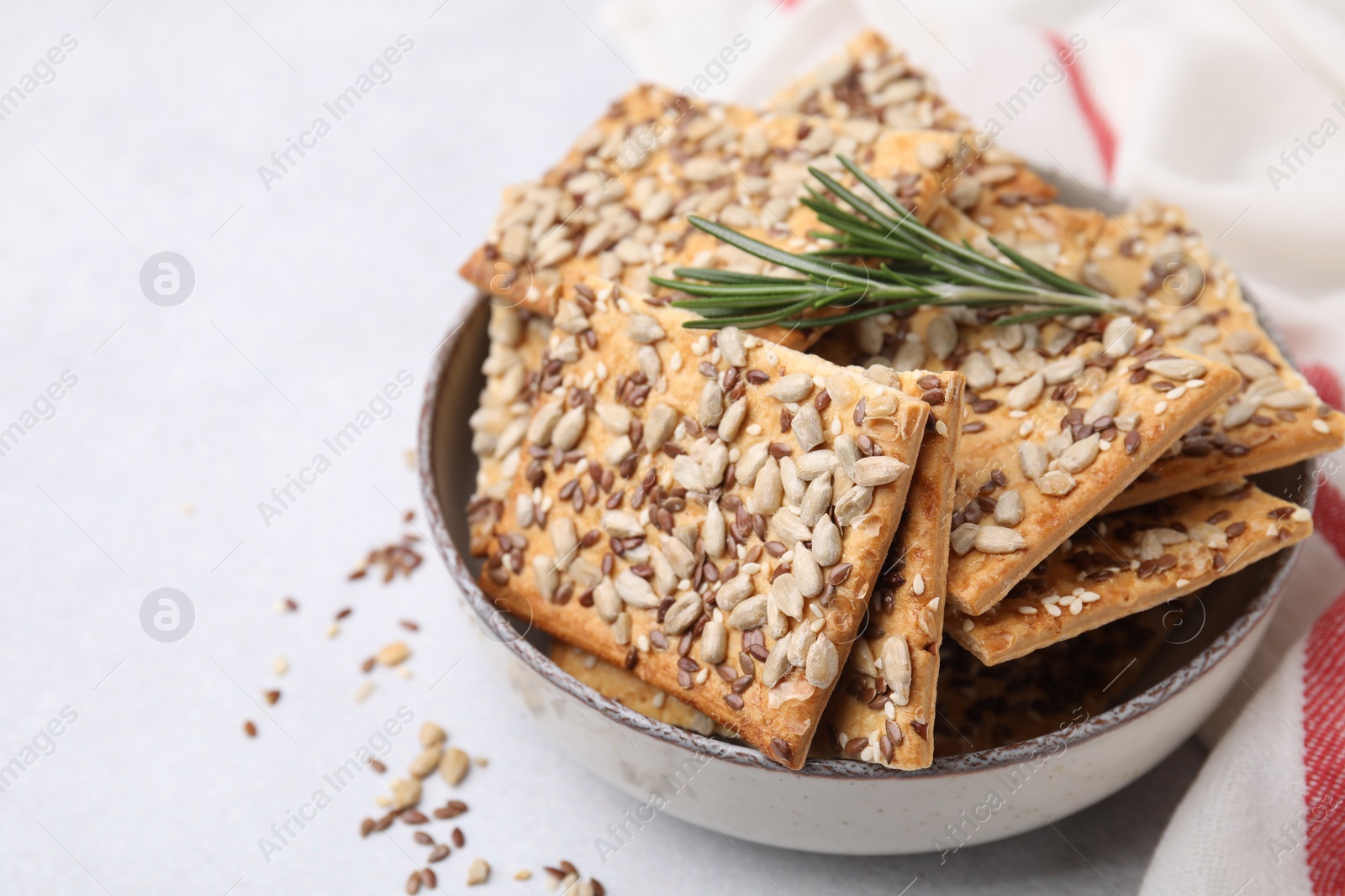 Photo of Cereal crackers with flax, sunflower, sesame seeds and rosemary in bowl on white table, closeup. Space for text