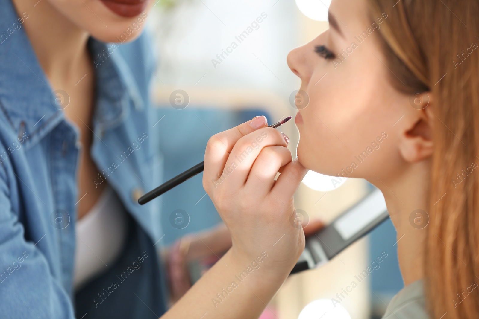 Photo of Professional visage artist applying makeup on woman's face in salon, closeup