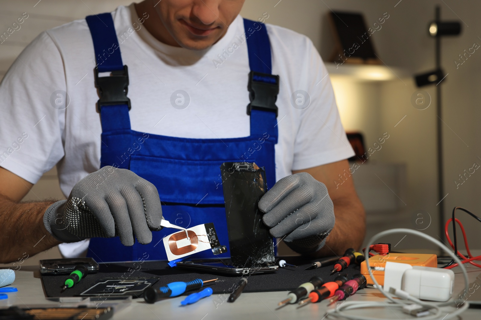 Photo of Technician repairing broken smartphone at table indoors, closeup