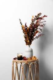 Photo of Vase with branches and candle on table near white wall