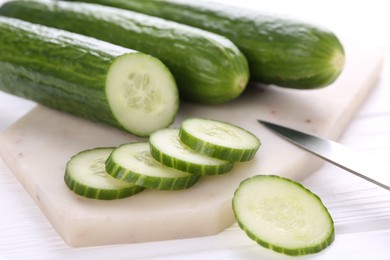 Cucumbers, knife and marble cutting board on white wooden table, closeup