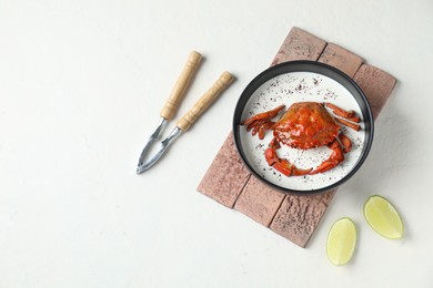 Delicious boiled crab with cream sauce and lime served on white table, flat lay. Space for text