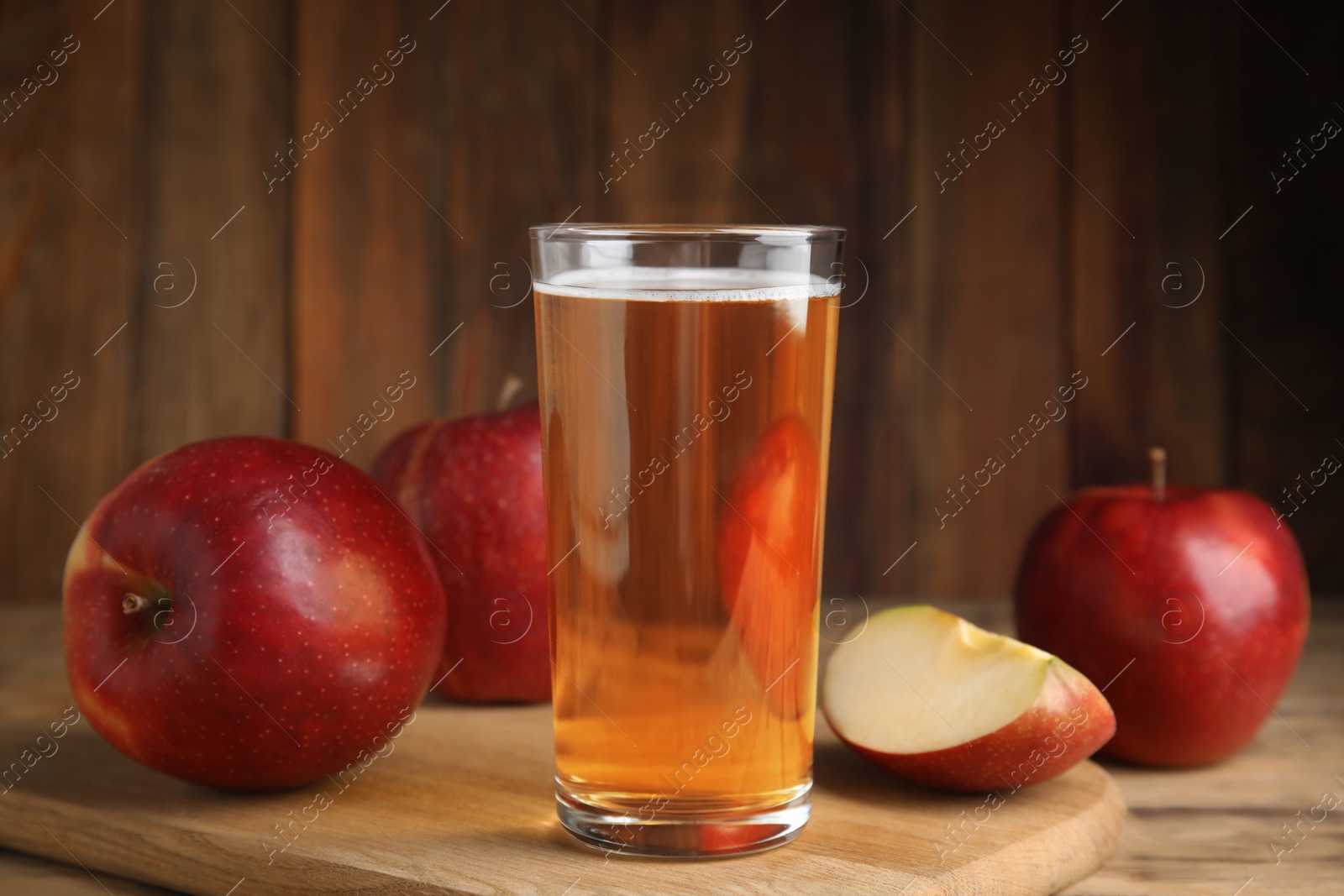 Photo of Glass of delicious cider and ripe red apples on wooden table