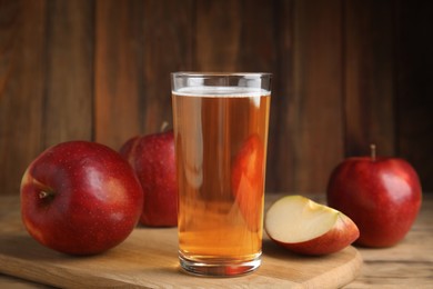 Photo of Glass of delicious cider and ripe red apples on wooden table
